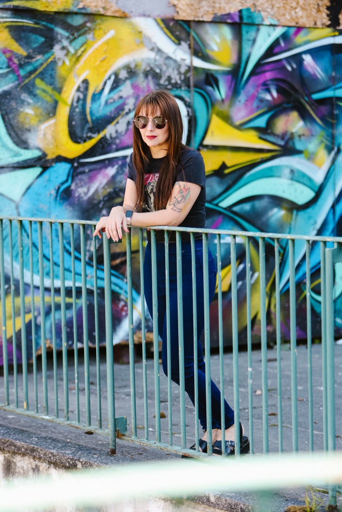 An image of Daniella, wedding business coach, standing in front of colourful graffiti wearing sunglasses